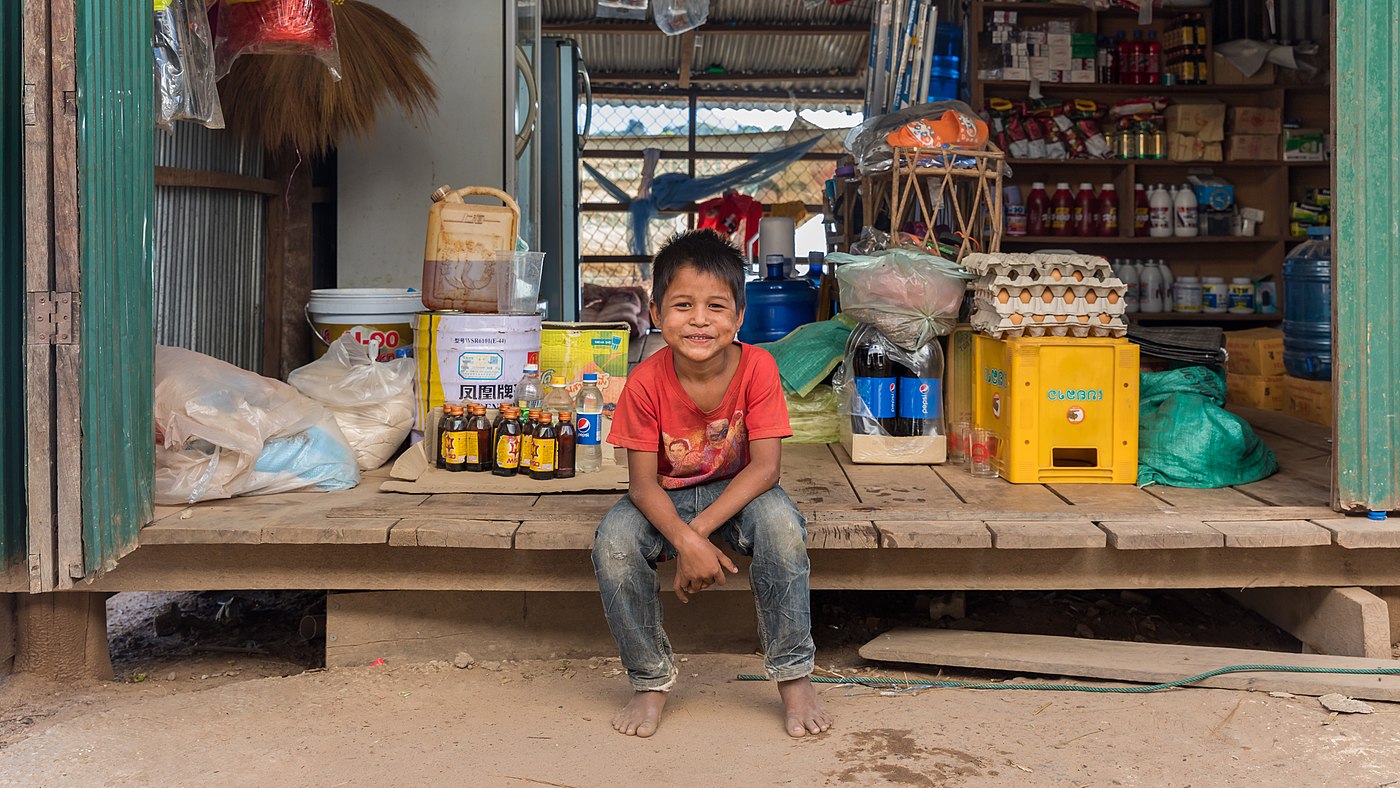 Jeune vendeur souriant assis dans une épicerie à Si Phan Don, Laos